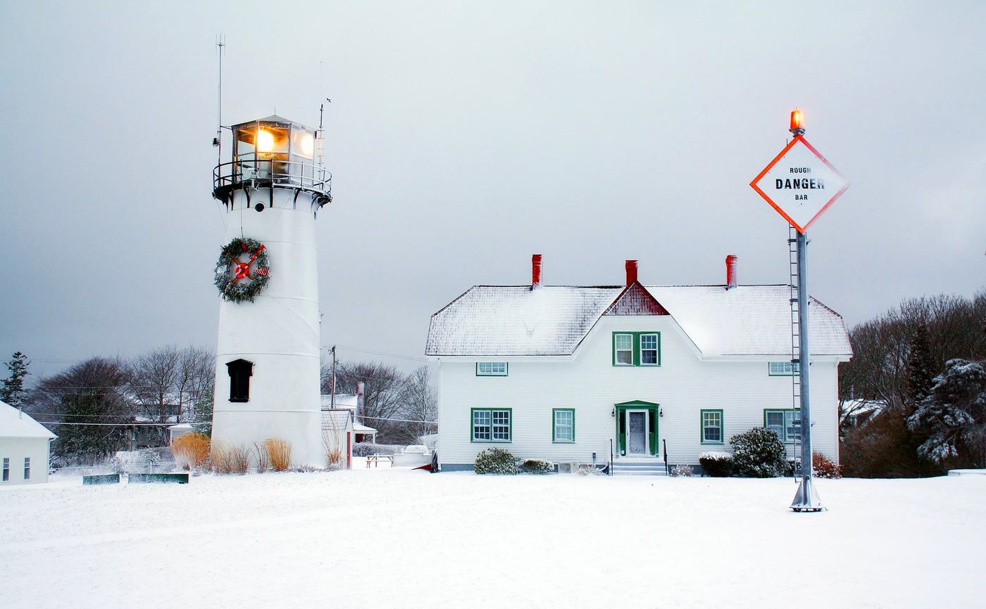 A Cape Cod lighthouse and keeper's house under snow on a grey winter afternoon.